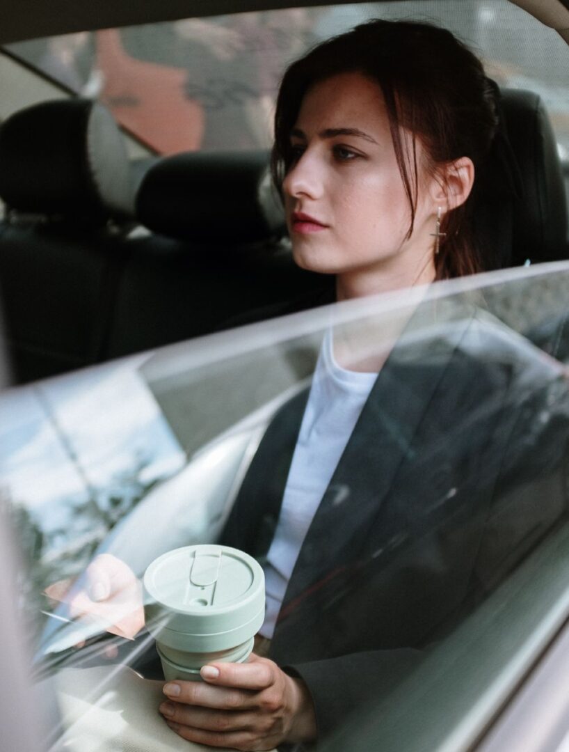 A woman sitting in the back of a car with a coffee.