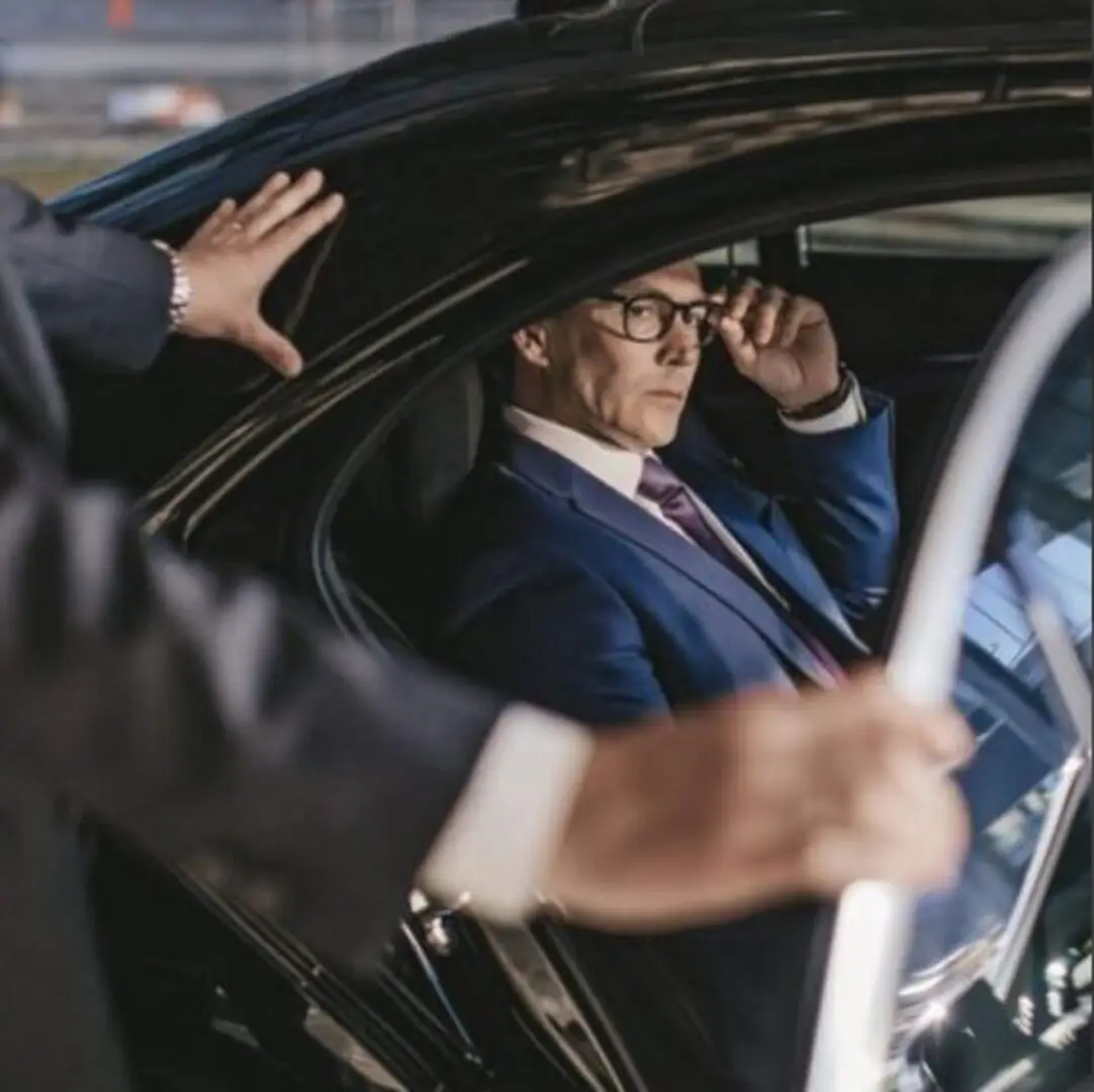 Businessman in a luxury car with chauffeur opening the door